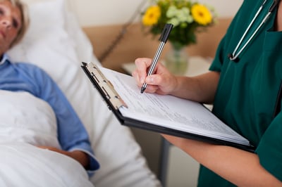 Writing on clipboard with patient in background in hospital-1