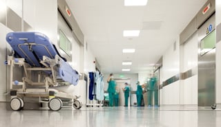 hospital hallway with a gurney in the foreground and blurry nurses in the background
